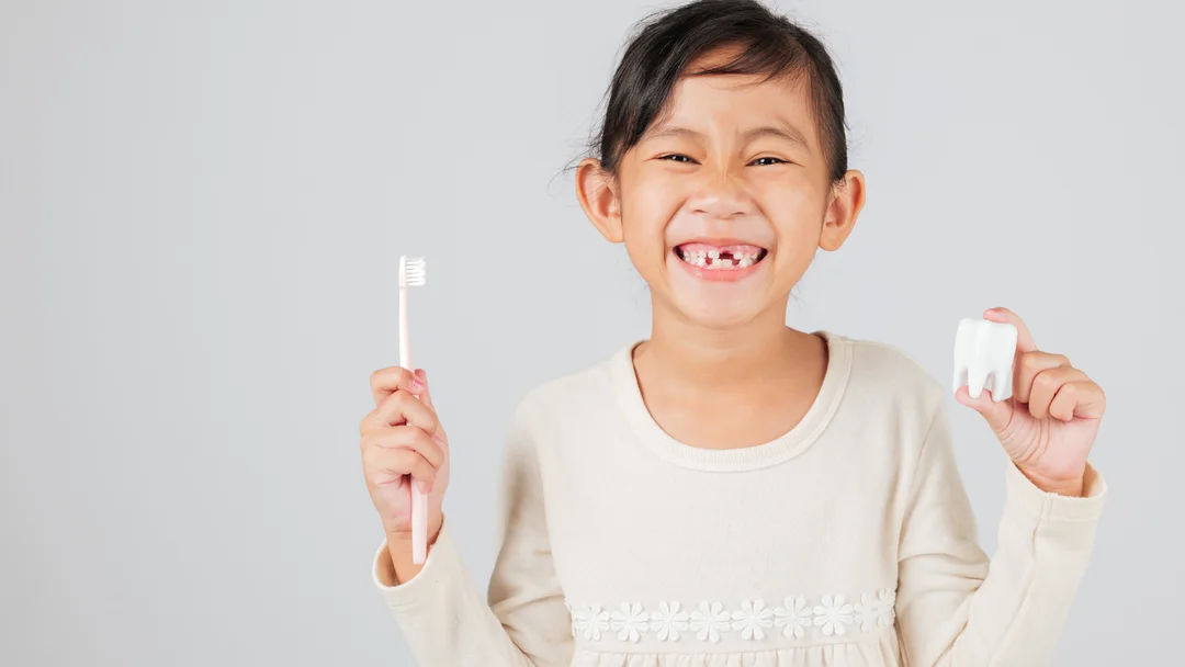 A young patient smiling at Five Star Dentistry, holding a toothbrush and a model tooth